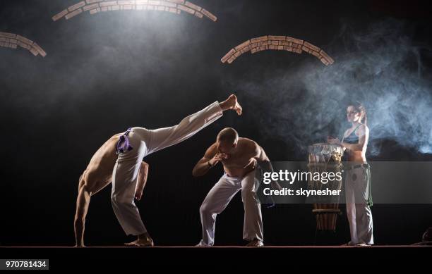 capoeira dancers having a sports training in a health club while woman is playing an instrument. - berimbau stock pictures, royalty-free photos & images