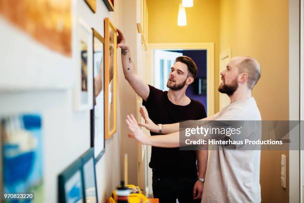 gay couple hanging pictures together - hanging picture frame stock pictures, royalty-free photos & images