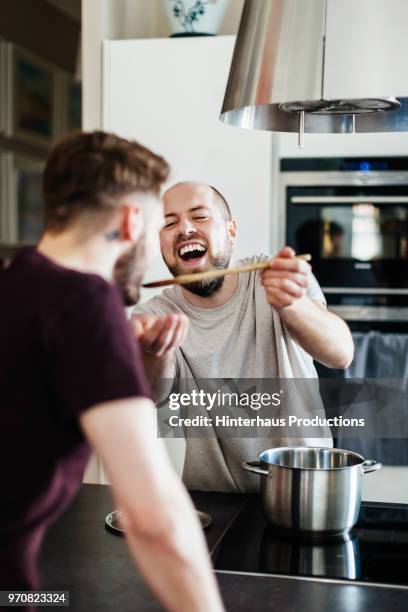 man laughing while partner tastes his cooking - spoon feeding stockfoto's en -beelden