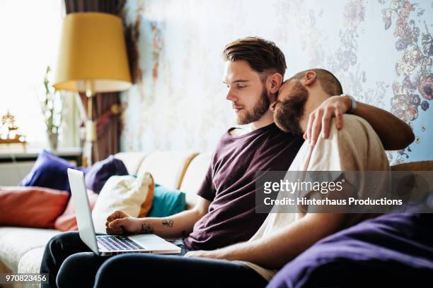 gay couple embracing on couch together - hinterhaus stockfoto's en -beelden