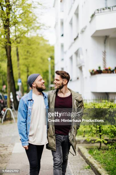gay couple talking while walking down street together - hinterhaus stockfoto's en -beelden