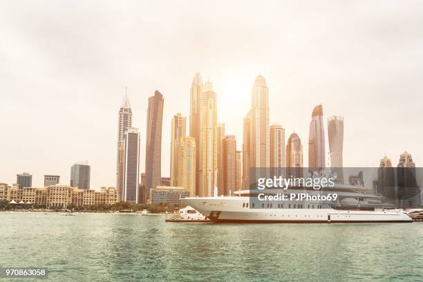 skyline of dubai from sea at sunset with a luxury yacht in foreground - pjphoto69 stock pictures, royalty-free photos & images