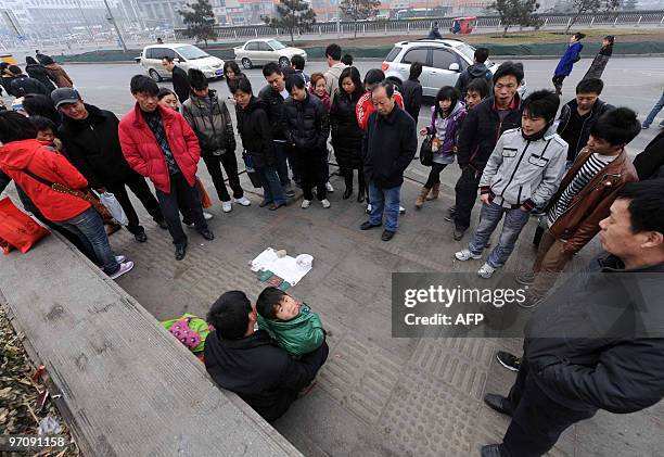 Homeless Chinese man attracts a crowd as he offers his six-year-old daughter up for adoption along a street in Beijing on February 25, 2010. In China...