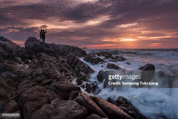 couple sitting on the rock and watching sunset at the beautiful  golden twilight. - negombo stockfoto's en -beelden