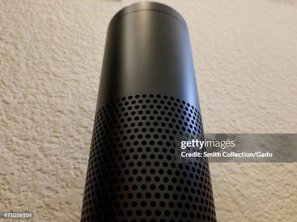 Low-angle, close-up view of Amazon Echo smart speaker using the Alexa service against a white wall in a home setting, suggesting an ominous or...