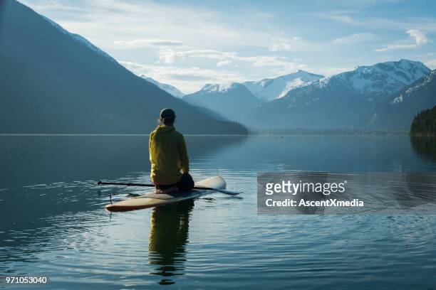 woman stand up paddle boarding on a pristine mountain lake - british columbia stock pictures, royalty-free photos & images