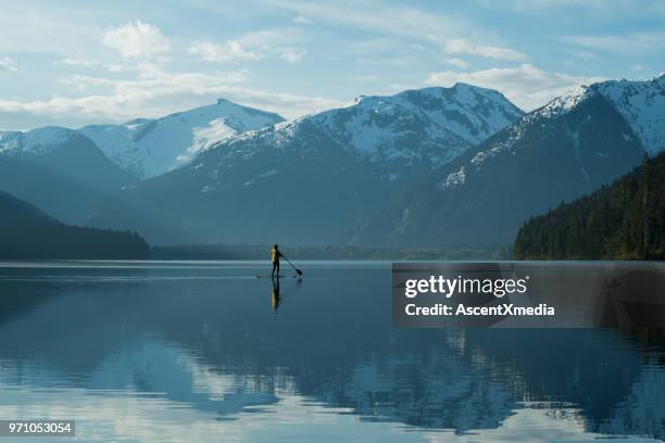 vrouw stand-up paddle instappen op een ongerepte bergmeer - british columbia coast mountains stockfoto's en -beelden