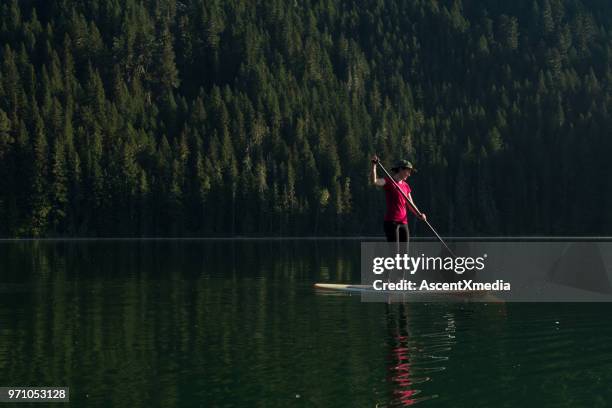 woman stand up paddle boarding on a pristine mountain lake - coast ranges stock pictures, royalty-free photos & images