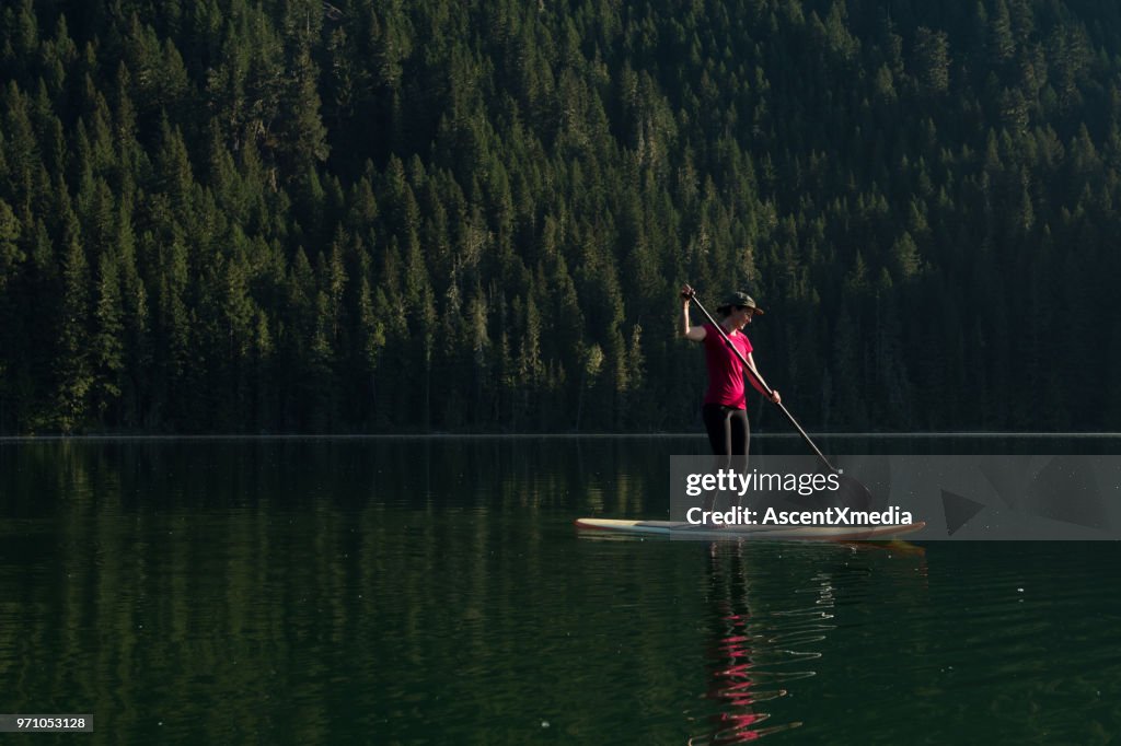 Woman stand up paddle boarding on a pristine mountain lake