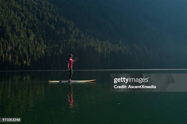 woman stand up paddle boarding on a pristine mountain lake - coast ranges stock pictures, royalty-free photos & images