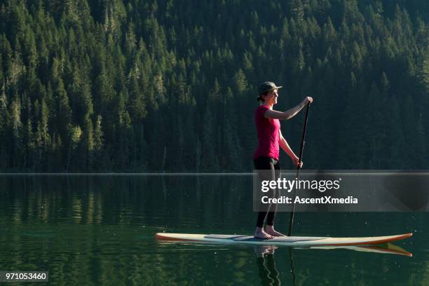 woman stand up paddle boarding on a pristine mountain lake - british columbia coast mountains stock pictures, royalty-free photos & images