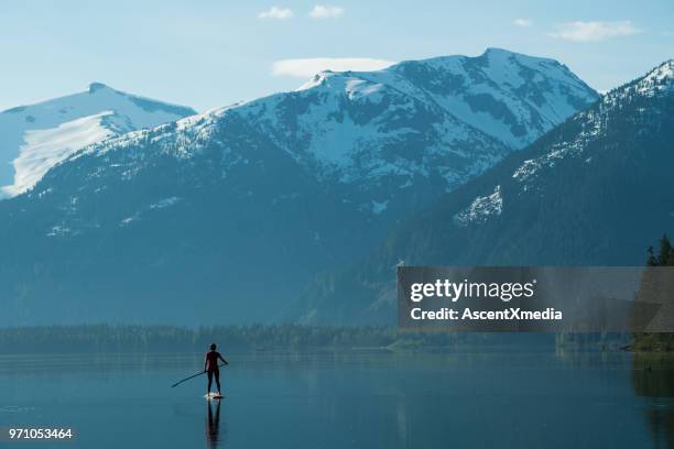 vrouw stand-up paddle instappen op een ongerepte bergmeer - british columbia coast mountains stockfoto's en -beelden