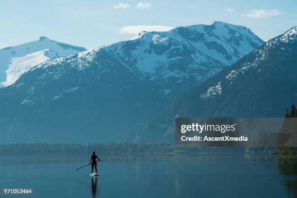 woman stand up paddle boarding on a pristine mountain lake - british columbia coast mountains stock pictures, royalty-free photos & images