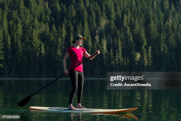 vrouw stand-up paddle instappen op een ongerepte bergmeer - british columbia coast mountains stockfoto's en -beelden