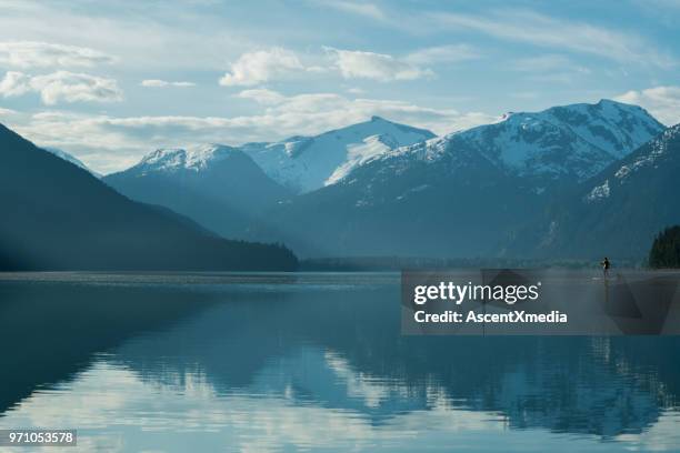 woman stand up paddle boarding on a pristine mountain lake - british columbia coast mountains stock pictures, royalty-free photos & images