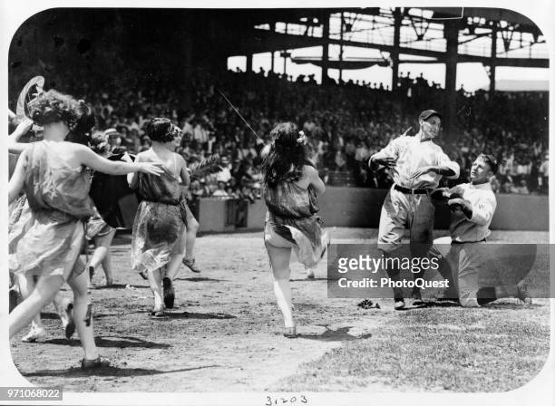 Group of costumed women dancing along a baseline as two unidentified baseball from the Washington National clown about, Washington DC, 1924.