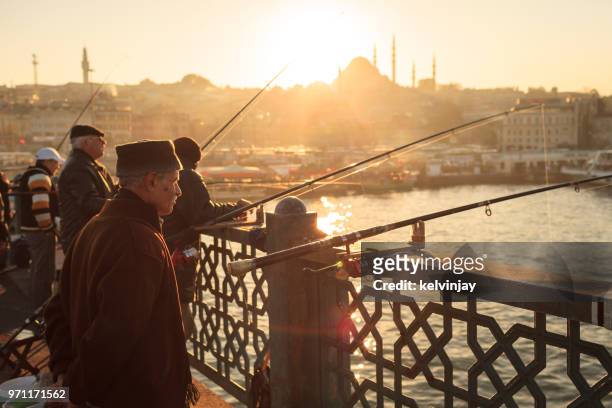 männer angeln bei sonnenuntergang auf der galata-brücke, istanbul, türkei - kelvinjay stock-fotos und bilder