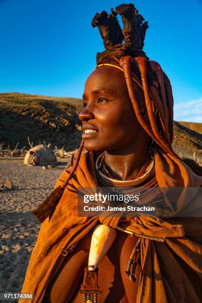red ochred, bare breasted himba woman in traditional dress looking into the distance, in the evening light, puros village, near sesfontein, namibia (model release) - himba stock-fotos und bilder