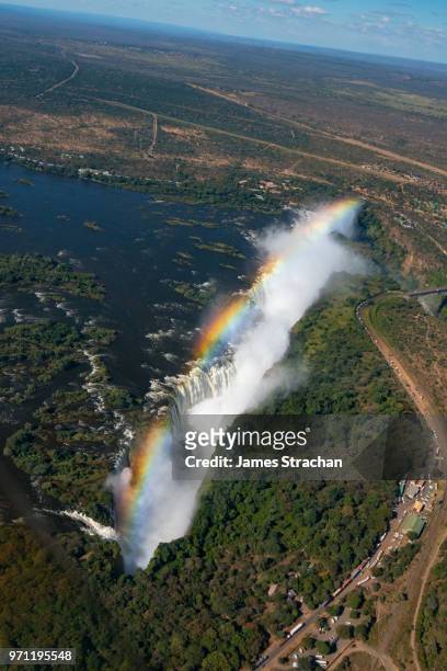 aerial view of the victoria falls framed by a rainbow pouring down, with spray rising high since the waters of the zambezi river are in full flood, zimbabwe - james strachan stock pictures, royalty-free photos & images