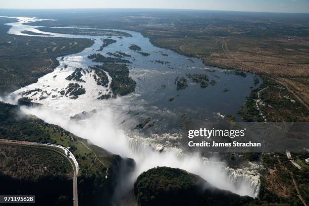 aerial view of the victoria falls pouring down with spray rising high since the waters of the zambezi river are in full flood, zimbabwe - james strachan stock pictures, royalty-free photos & images