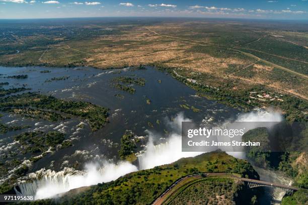 aerial view of the victoria falls pouring down with spray rising high since the waters of the zambezi river are in full flood, zimbabwe - james strachan stock pictures, royalty-free photos & images