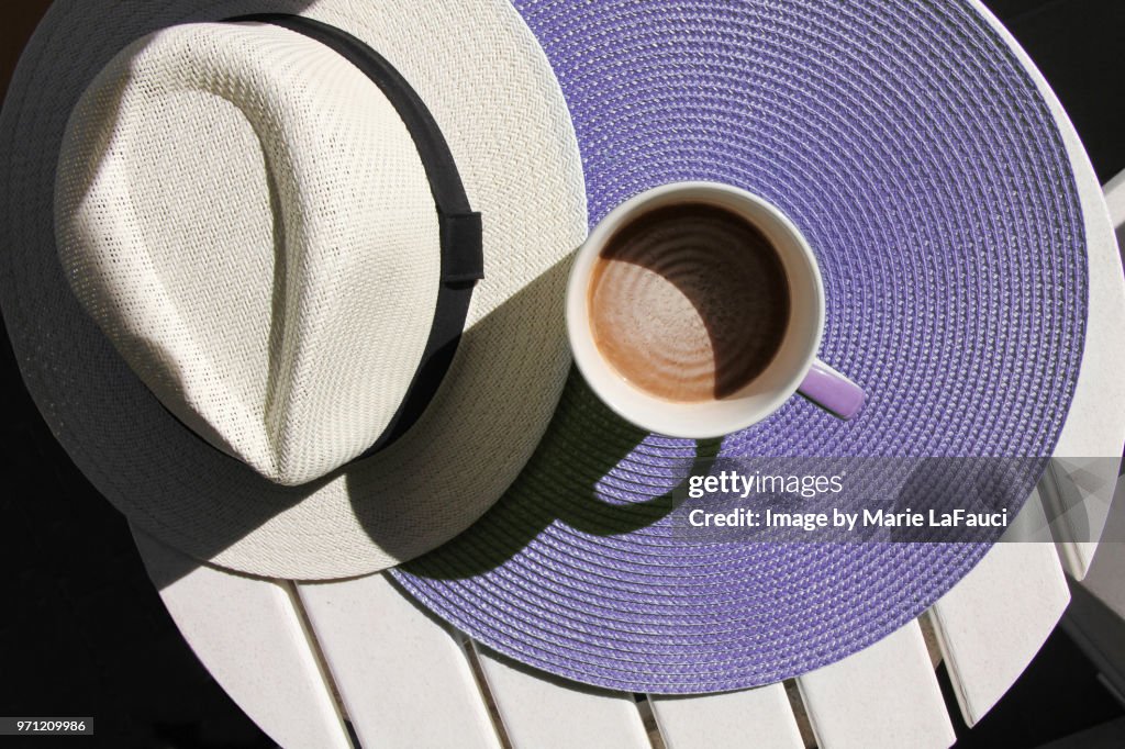 Top view of coffee cup with straw hat on purple placemat