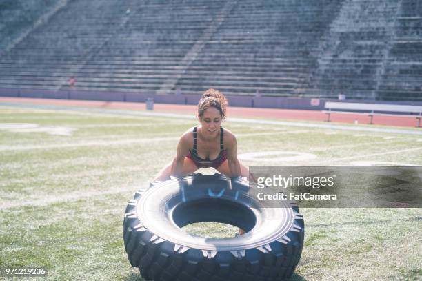 female athlete cross trains with a giant tire on a stadium field - unapologetic stock pictures, royalty-free photos & images