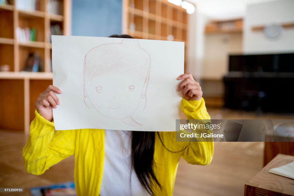 Young girl holding a self drawn portrait in front of her face