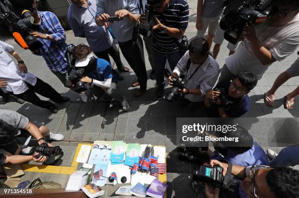 Members of the media take photographs and video footage of North Korean and American flags and books displayed for sale at a stall outside the St....