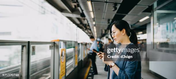 young woman using mobile phone in subway station platform - waiting for train stock pictures, royalty-free photos & images