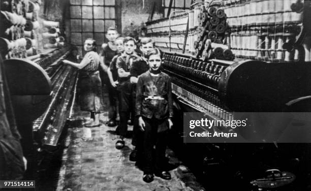 Old black and white archival photograph showing female worker and child labourers posing in spinning mill in the early twentieth century.