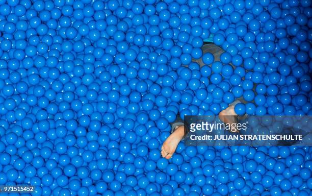 Trade fair visitor lies headfirst in a blue ball bath at the IBM stand at the Cebit technology fair in Hanover, Germany on June 11, 2018. - The...