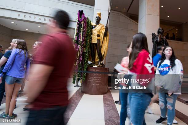 Tourists pass by Hawaii's King Kamehameha statue draped in long strands of lei in the Capitol Visitor Center on Kamehameha Day, Monday, June 11, 2018.