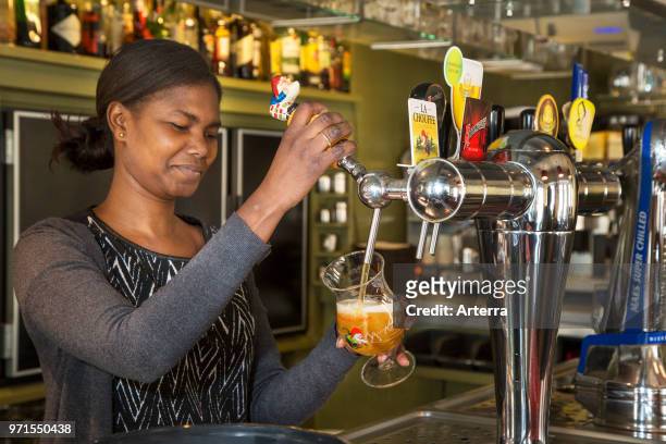 Black barmaid drawing Belgian draught beer in glass in Flemish tavern De Gulden Cop in the town Temse / Tamise, East Flanders, Belgium.
