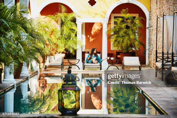 woman in robe sitting in lounge chair by hotel pool while working on smartphone - hotel de lujo fotografías e imágenes de stock