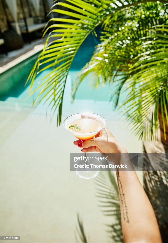 Woman holding drink with resort pool and palm fronds in background