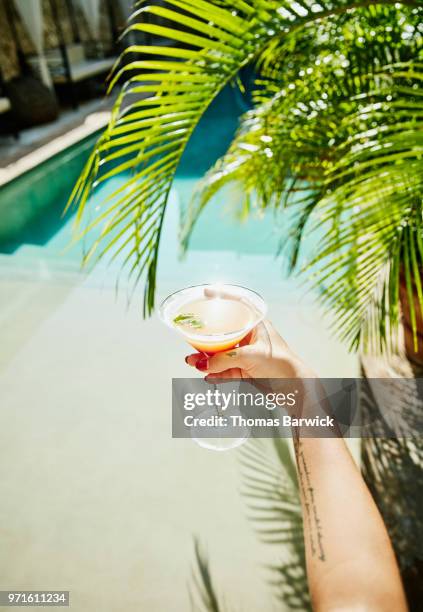 woman holding drink with resort pool and palm fronds in background - swimming pool and hand stock pictures, royalty-free photos & images