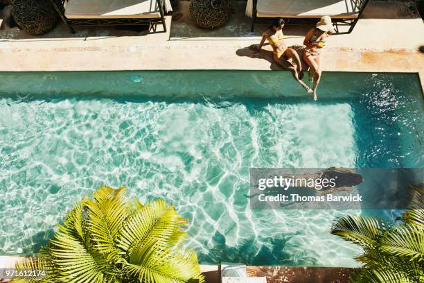 overhead view of female friends seated next to outdoor hotel pool as friend swims underwater - luxushotel stock-fotos und bilder