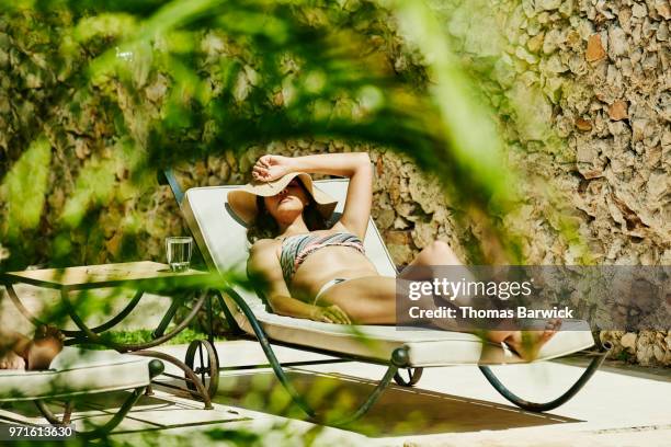 woman in sun hat relaxing in lounge chair by pool enjoying the sun - women sunbathing stock pictures, royalty-free photos & images