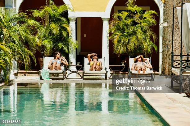 female friends relaxing together in lounge chairs by pool in boutique hotel courtyard - sólo con adultos fotografías e imágenes de stock