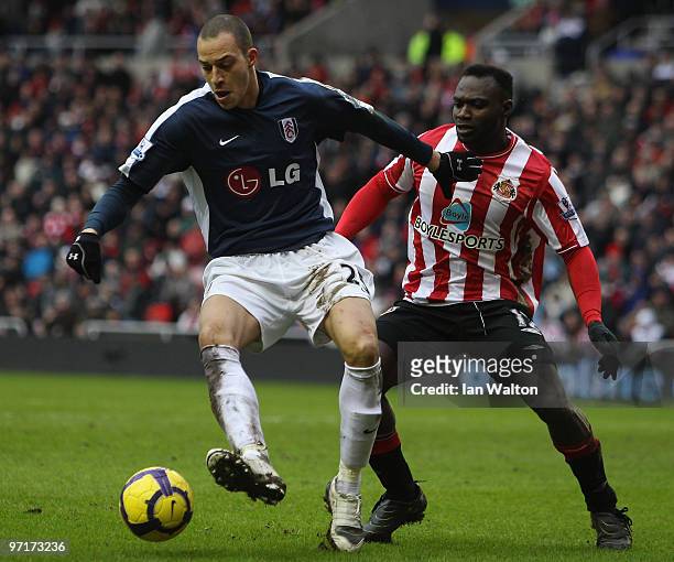 John Mensah of Sunderland tries to tackle Bobby Zamora of Fulham during the Barclays Premier League match between Sunderland and Fulham at Stadium of...