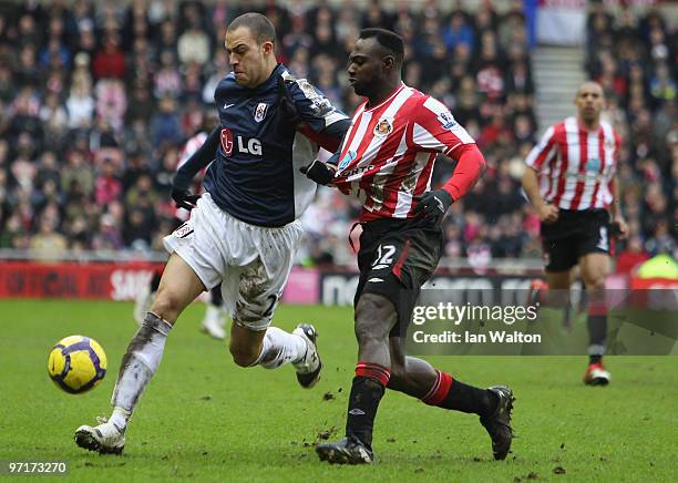 John Mensah of Sunderland tries to tackle Bobby Zamora of Fulham during the Barclays Premier League match between Sunderland and Fulham at Stadium of...