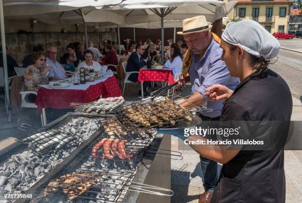 Restaurante Alfandega" cook is helped by a waitress while grilling sardines, beef and other fish over charcoal by Ave River on May 28, 2018 in Vila...