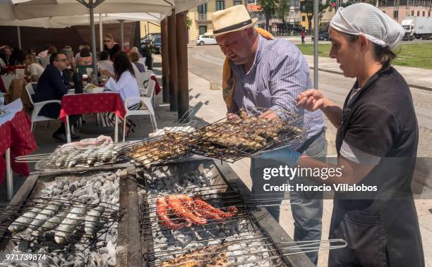 Restaurante Alfandega" cook is helped by a waitress while grilling sardines, beef and other fish over charcoal by Ave River on May 28, 2018 in Vila...