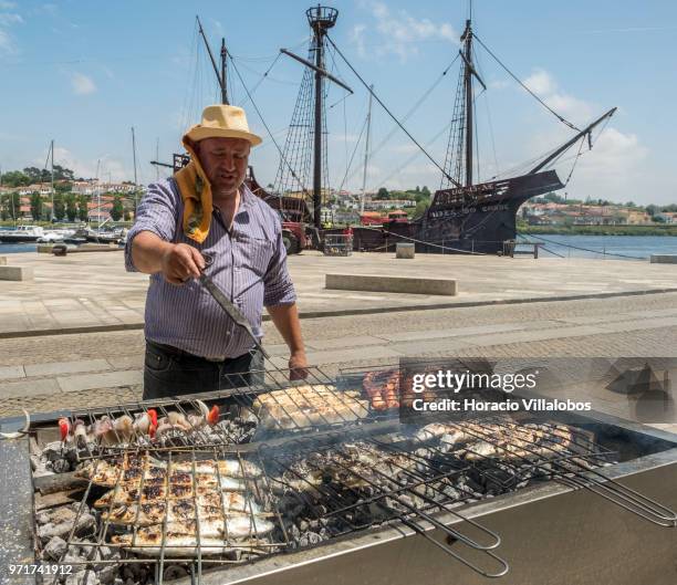 Replica of a Portuguese 16th century caravel is seen behind the "Restaurante Alfandega" cook grilling sardines, beef and other fish over charcoal by...