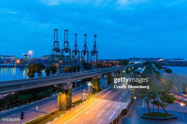 Vehicles drive across the Sentosa causeway bridge at dawn as gantry cranes stand at the Tanjong Pagar Container Terminal, operated by PSA...