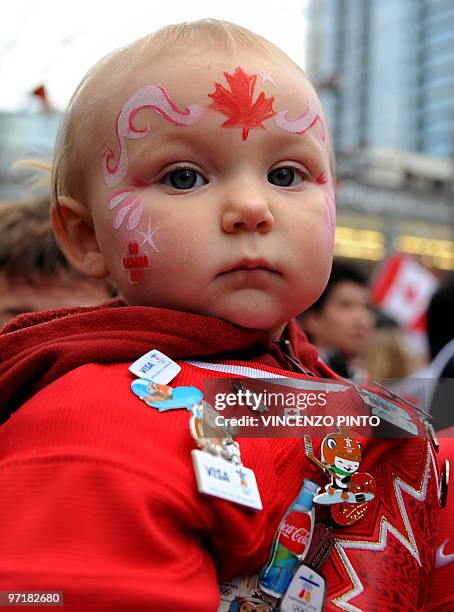 Baby with his face painted and pins on his shirt is carried as Canada supporters celebrate in downtown Vancouver following the Canadian's ice hockey...