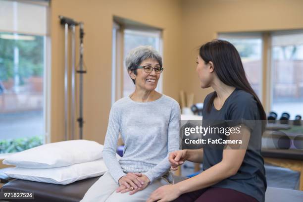 ein physiotherapeut spricht mit ihrem älteren patienten in einer klinik - koordination stock-fotos und bilder