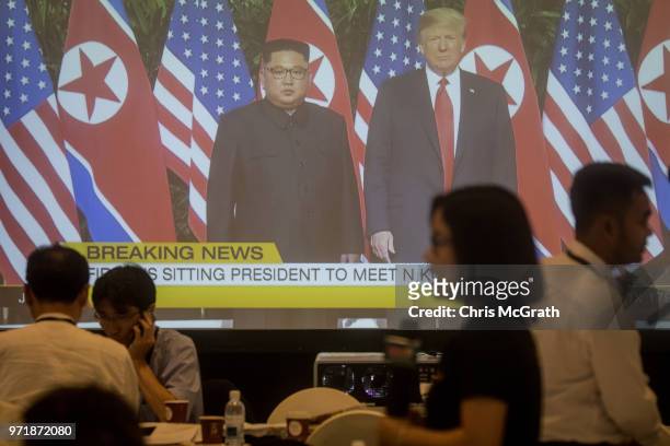 Members of the press work at the international press center in front of a big screen showing footage of the meeting between U.S. President Donald...