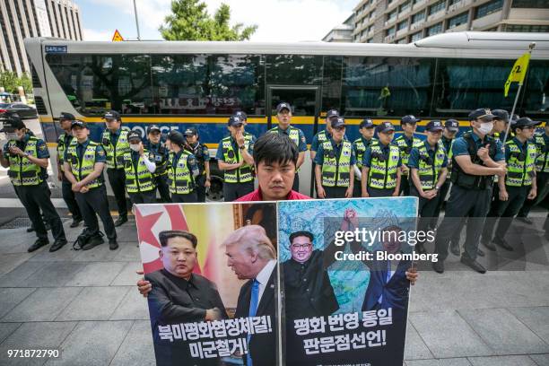 Police officers stand guard as a demonstrator holds placards featuring images of North Korean leader Kim Jong Un, U.S. President Donald Trump and...